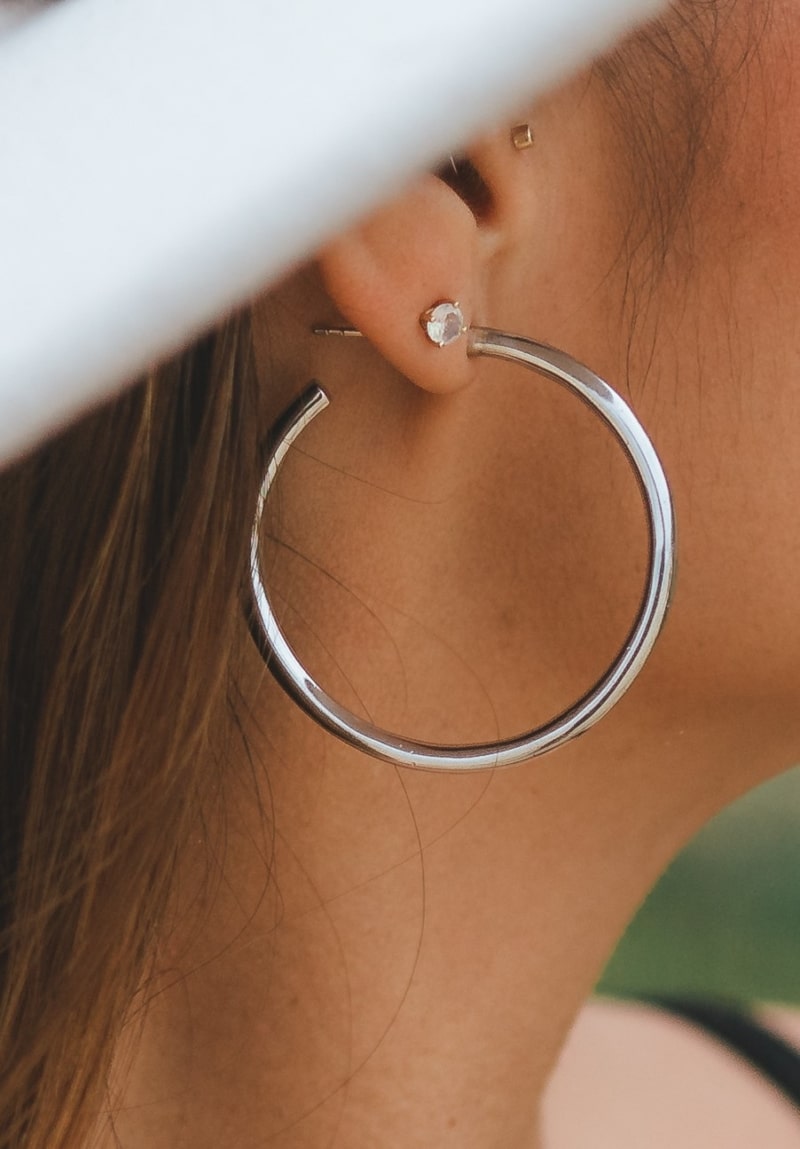washed ashore brand close-up of silver tide hoop earring and white saphhire stud earring
